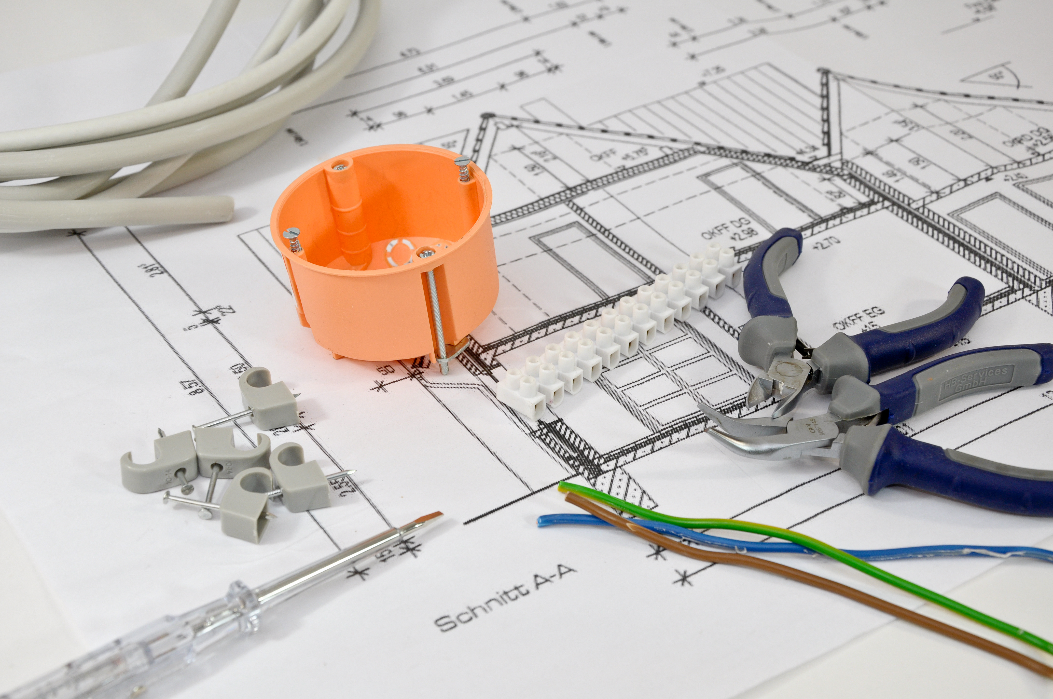 Auf der Querschnittszeichnung eines Hausneubaus liegen Werkzeuge zur Elektroinstallation.